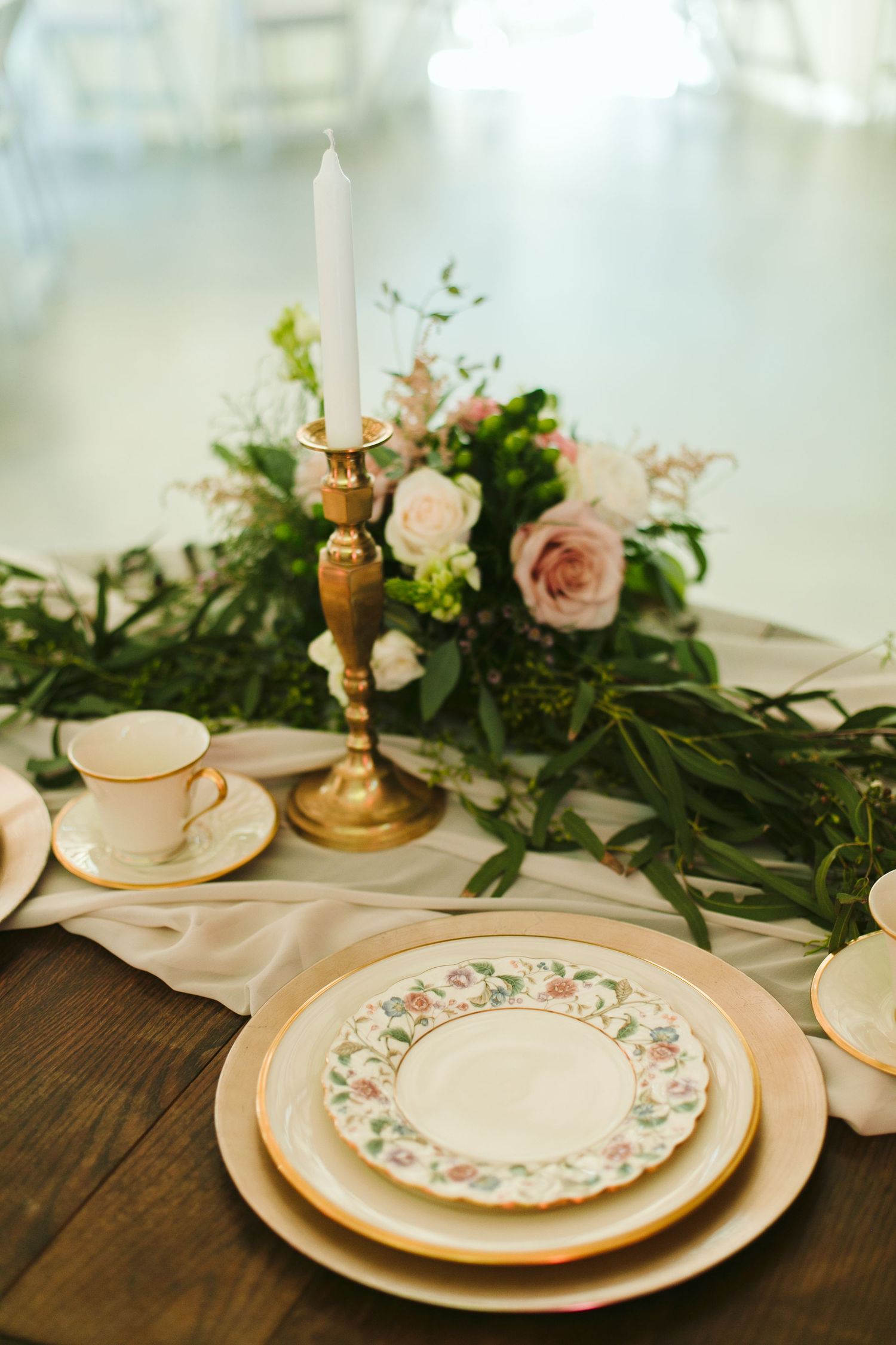 Elegant table setting with vintage china, gold candlestick and pink roses on wooden surface.