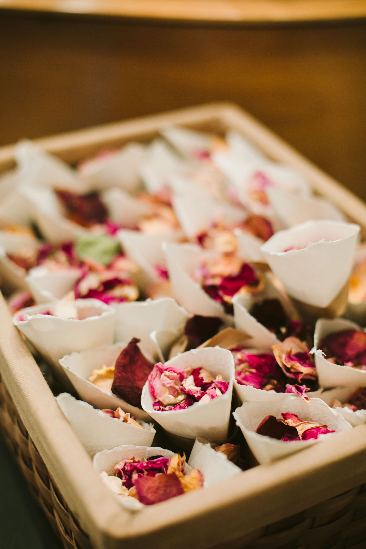 Wedding flower petals arranged in white paper cones on a wooden surface.