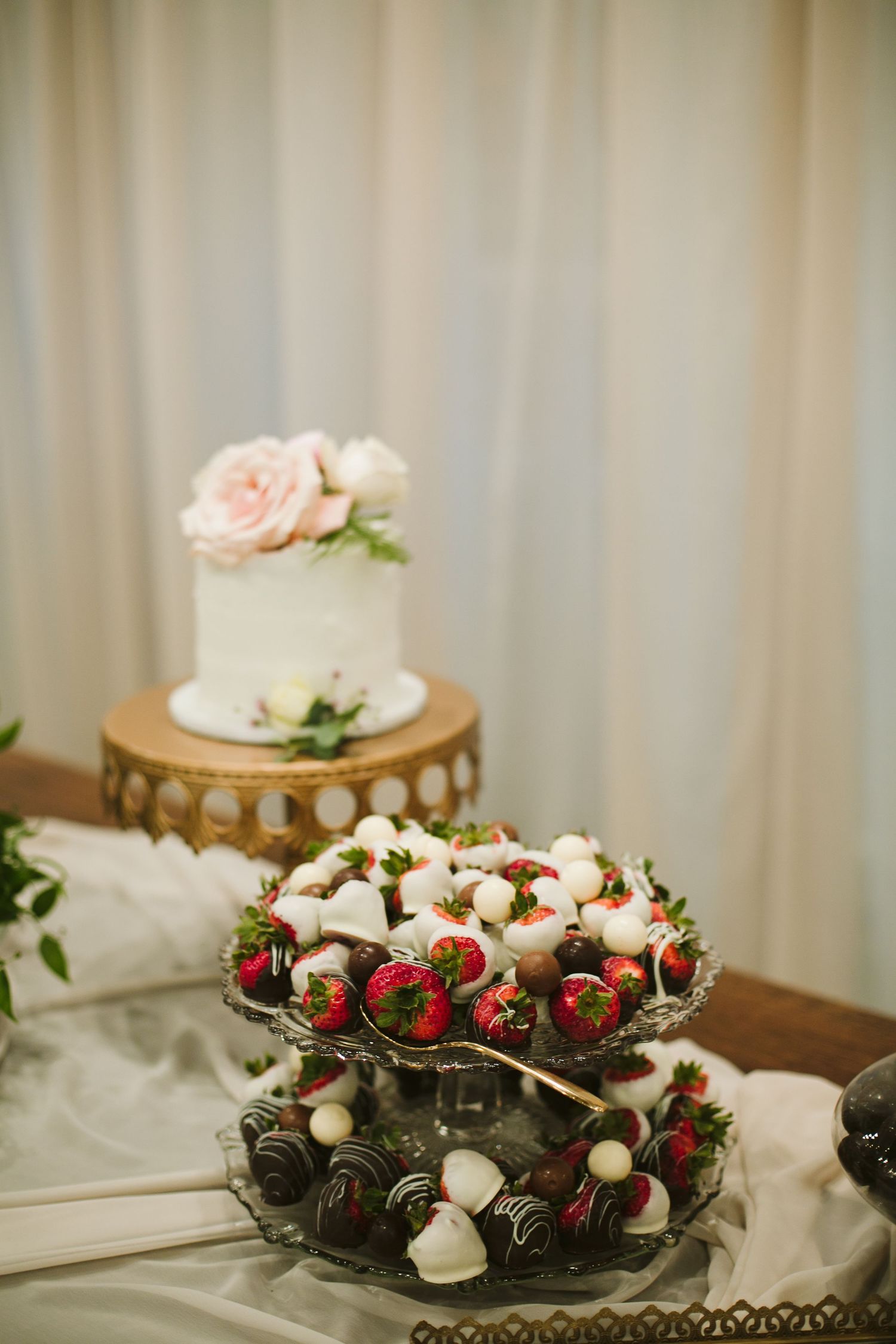 Elegant wedding dessert display featuring chocolate covered strawberries and simple white cake.