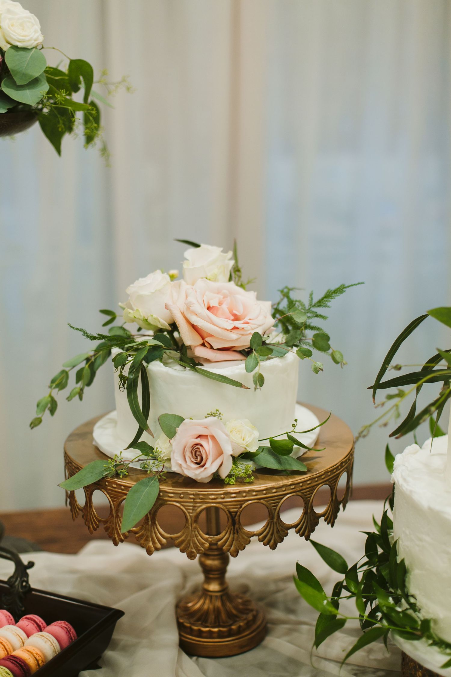 Elegant white wedding cake adorned with pink roses and greenery on a gold vintage cake stand.