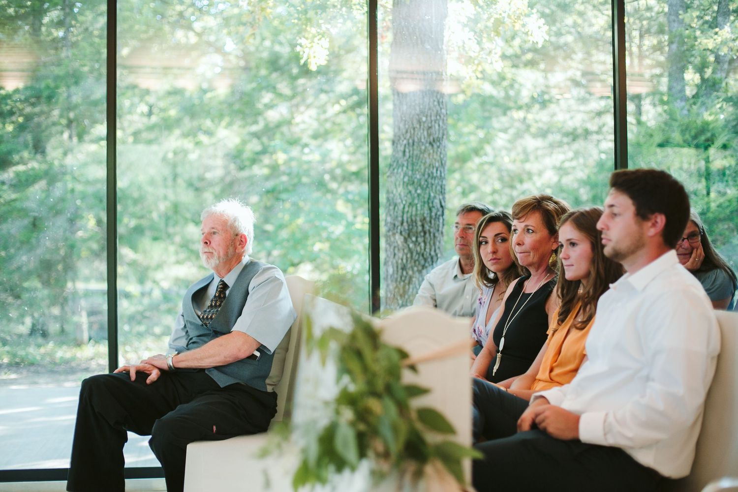 Wedding guests seated in a bright sunlit room with large windows during ceremony.