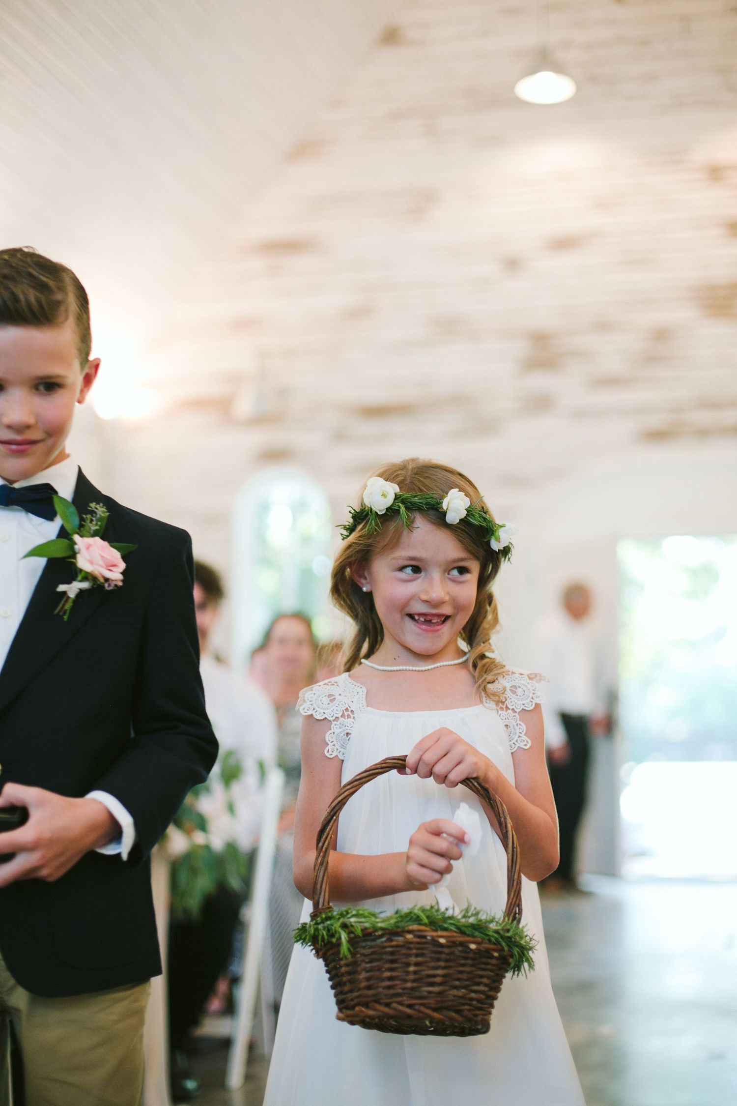 Young attendants in formal attire walk down the aisle, with one carrying a decorated basket.