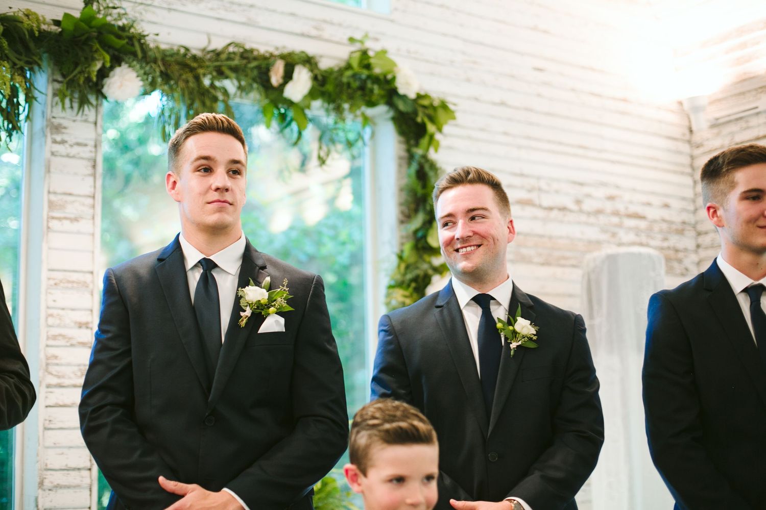 Wedding party standing at altar under greenery arch during ceremony.
