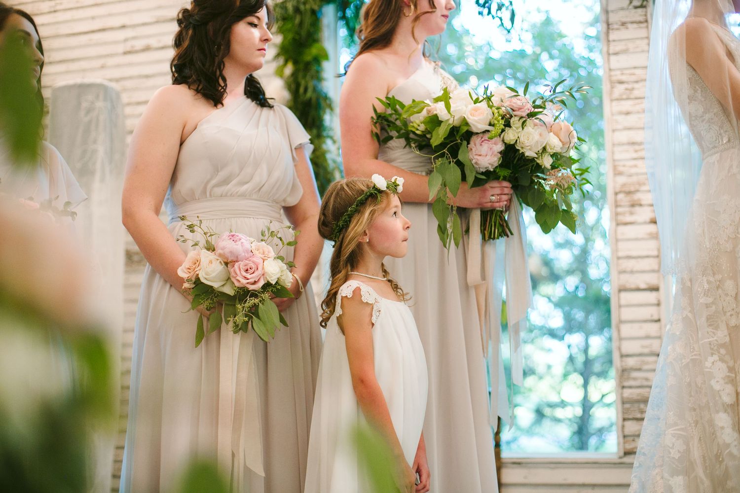 Wedding party members in light colored dresses stand together during the ceremony.