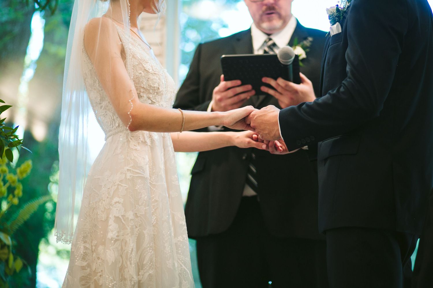 A close-up of hands during a wedding ceremony with an officiant holding a tablet.