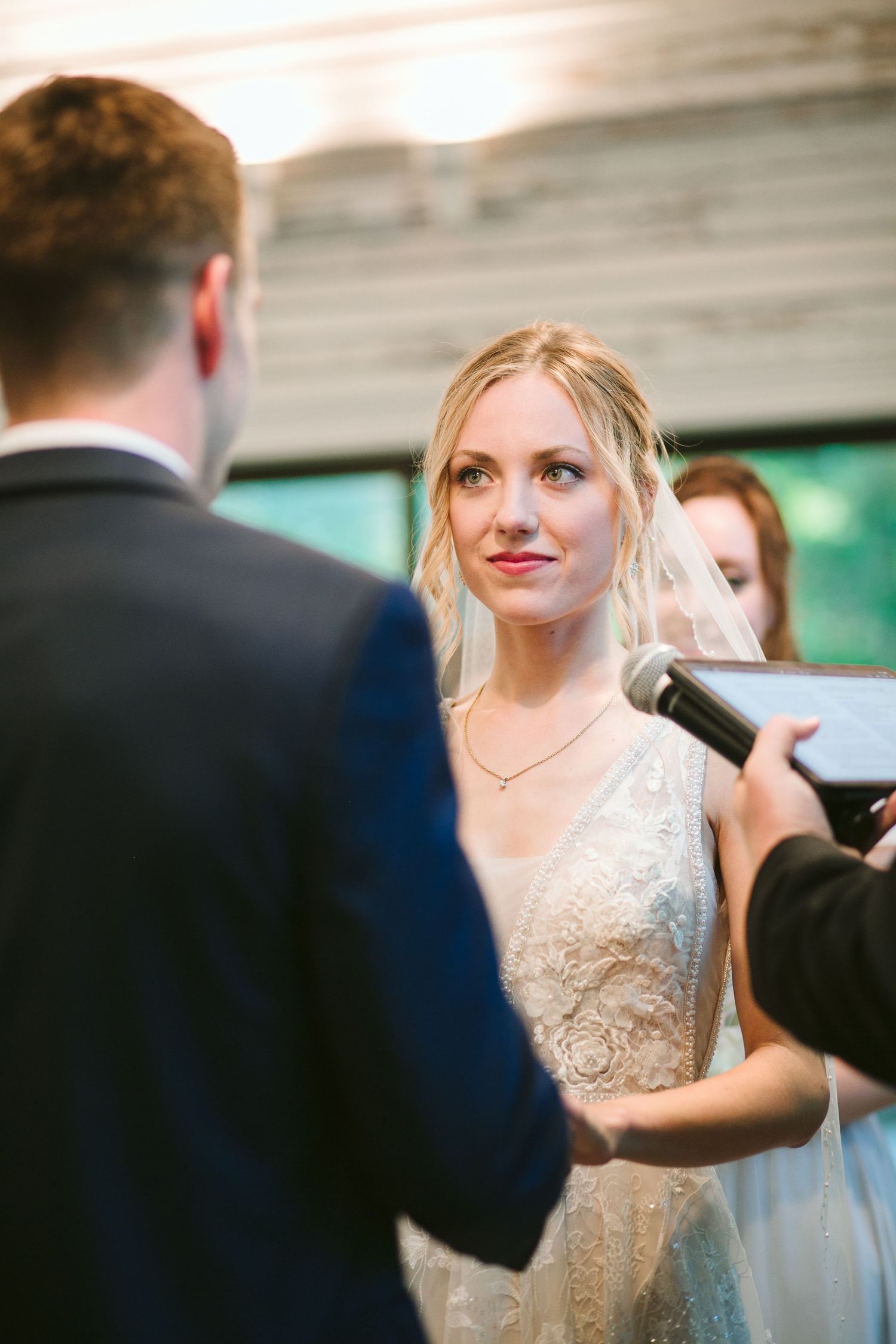 Bride in a delicate lace wedding dress smiles during the ceremony while exchanging vows.
