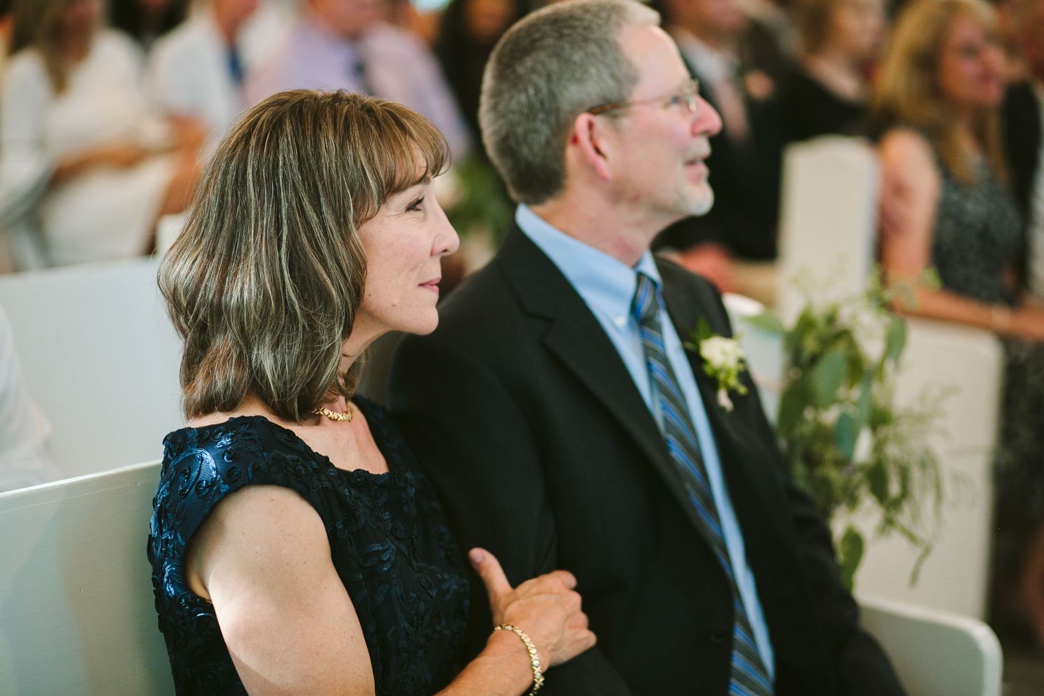 Wedding guests dressed in formal attire watch the ceremony with joyful expressions.