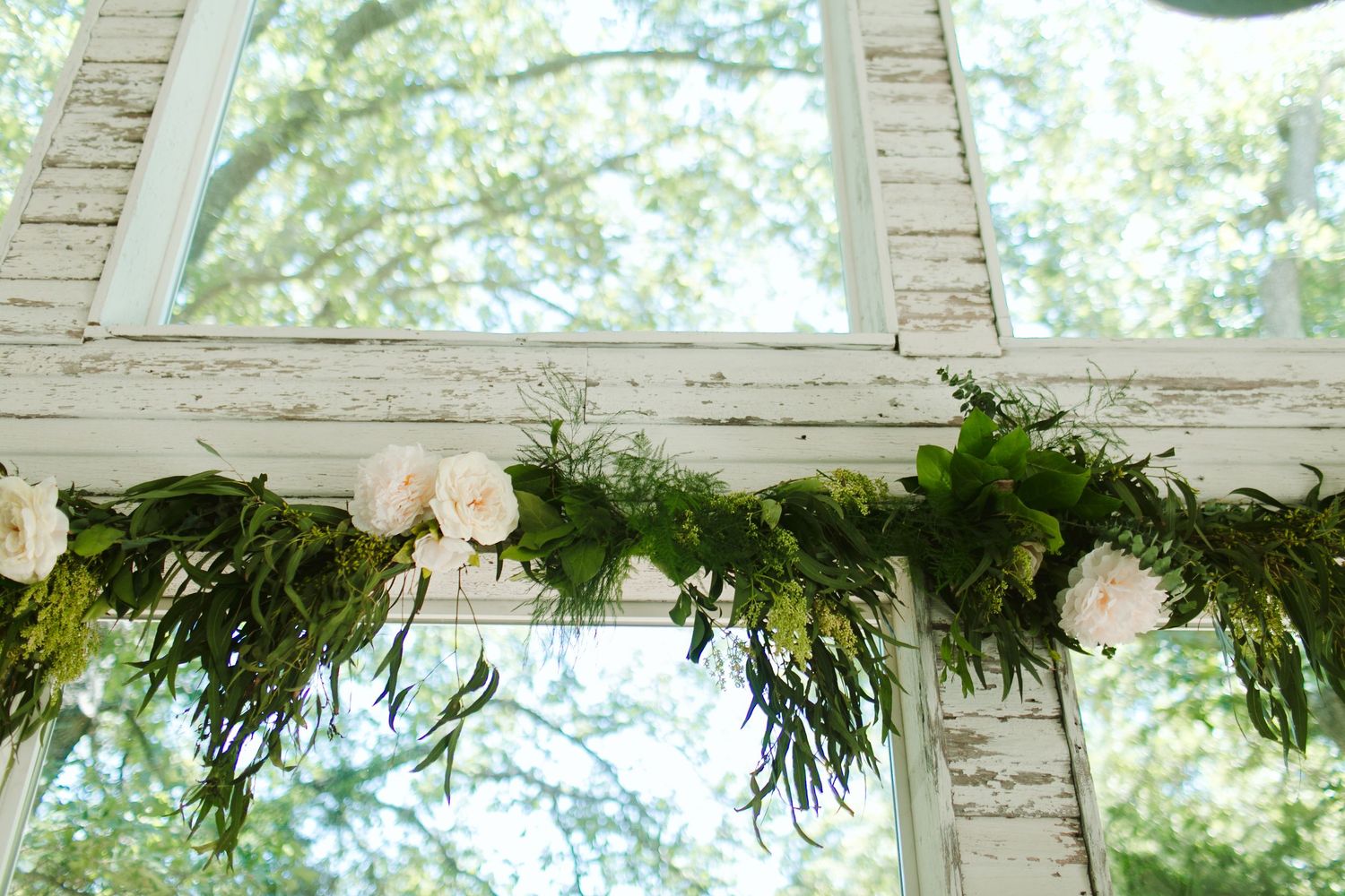 Lush greenery and white floral garland decorates white brick window frame.