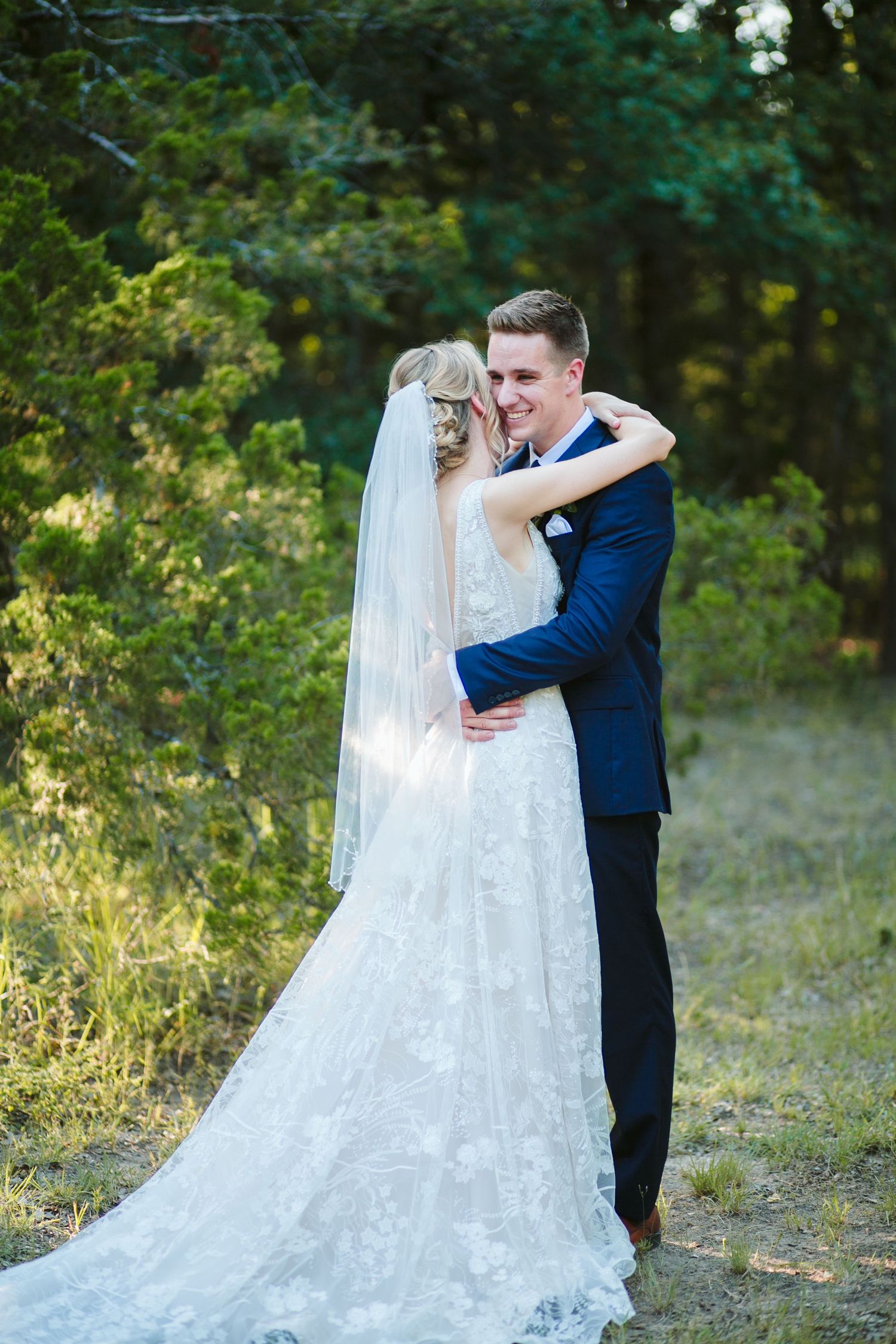Romantic embrace between newlyweds outdoors with bride wearing flowing lace gown.