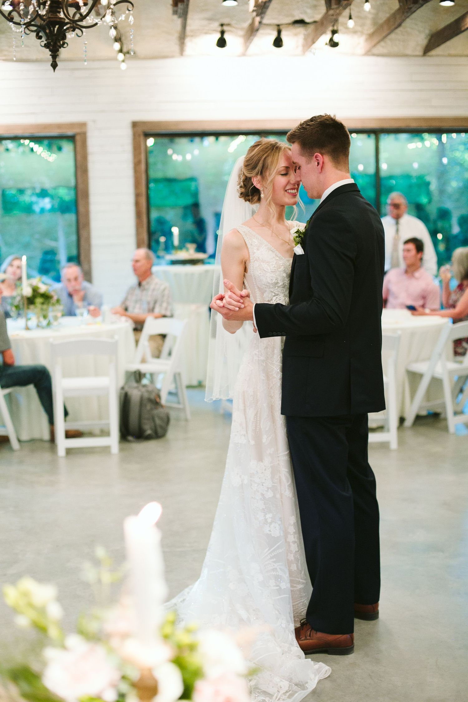 Romantic moment between newlyweds during first dance in rustic venue with string lights.