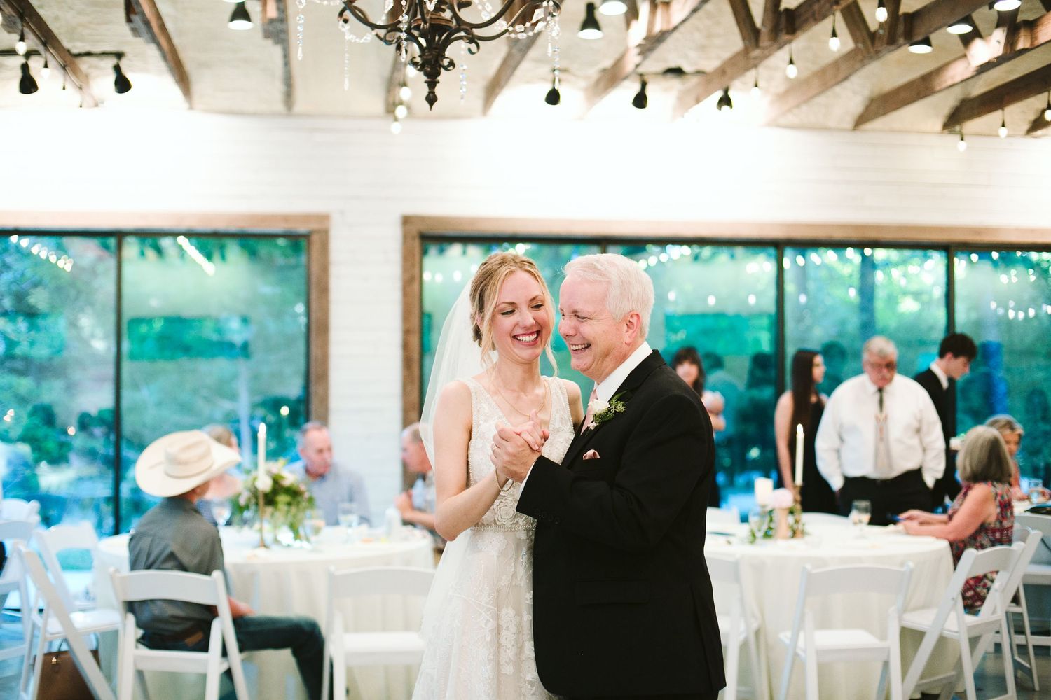 Wedding reception dance in a bright venue with white tables and teal wall art.