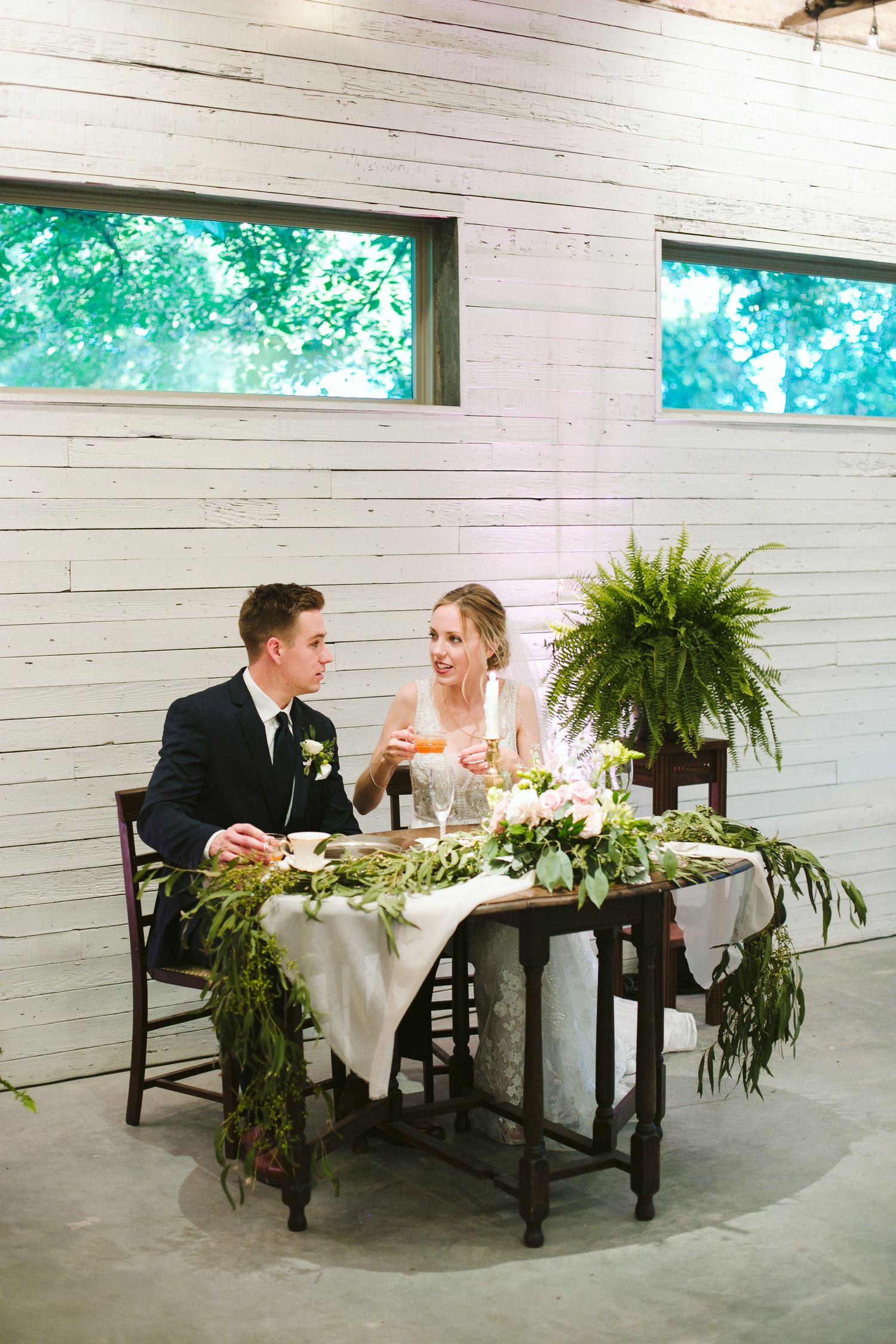 Newlyweds sharing moment at sweetheart table decorated with greenery garland.