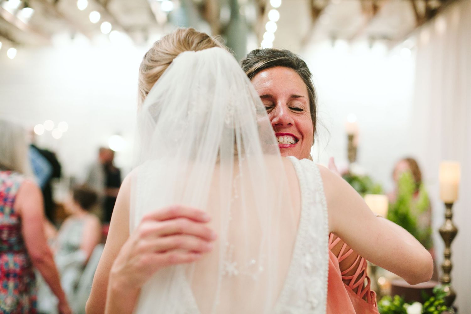 Joyful embrace shared during wedding celebration with white decor and candlelit ambiance.