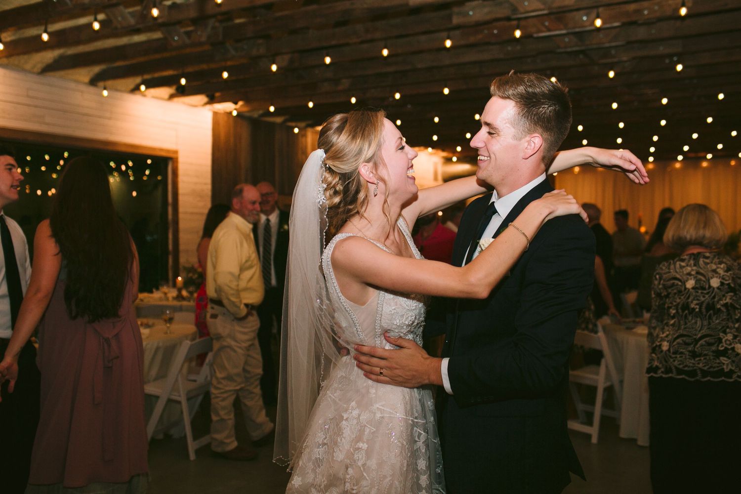 Wedding reception dance under romantic string lights in rustic venue.