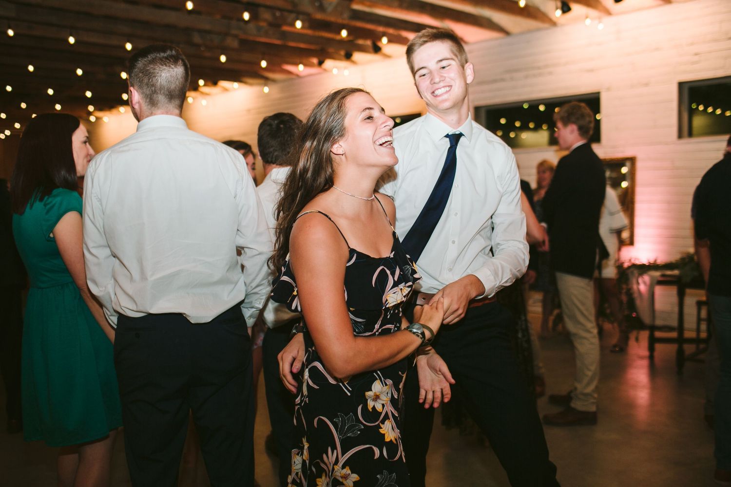Guests dancing and celebrating at wedding reception under string lights.