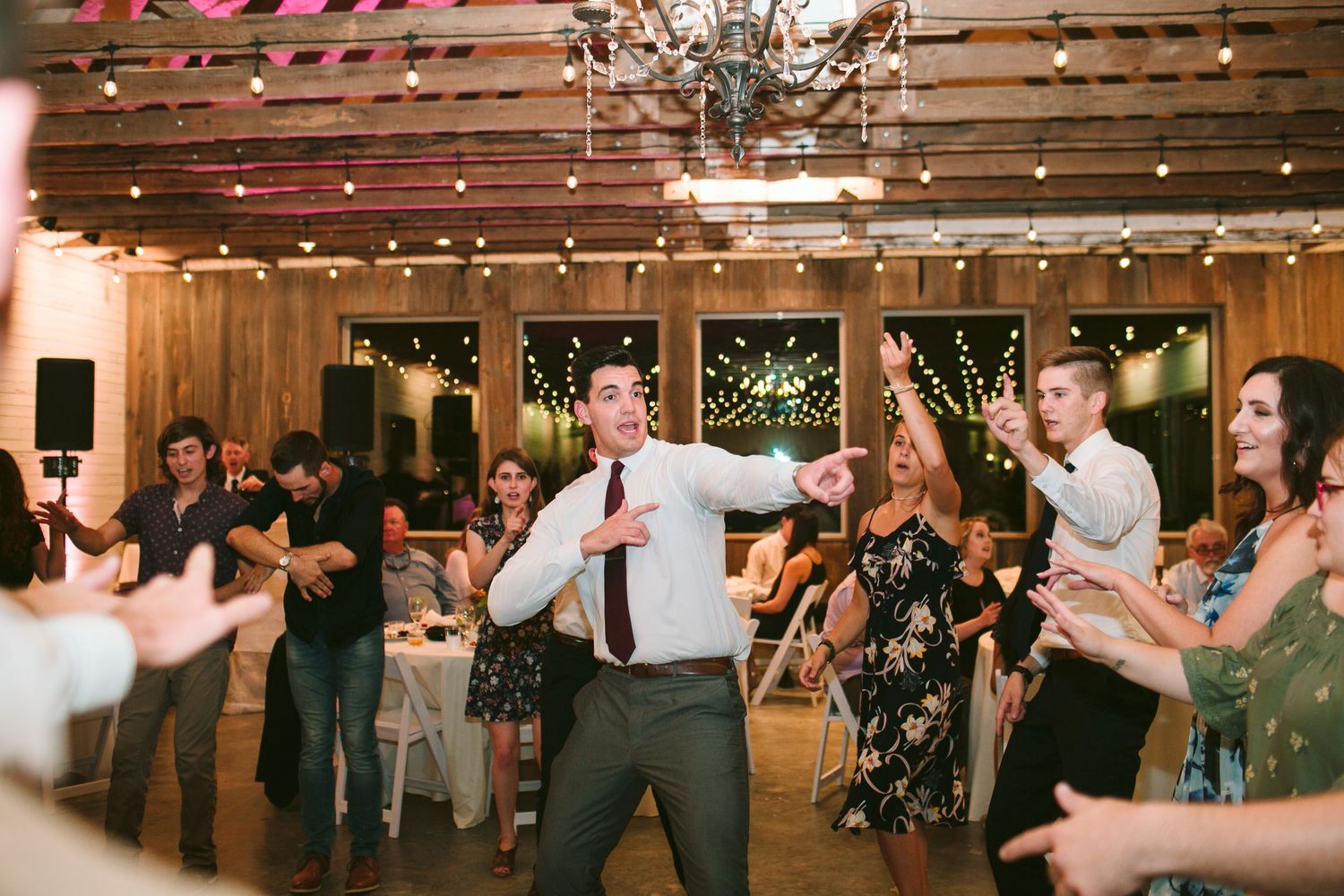 Lively dance party with guests celebrating under wooden beams and string lights.