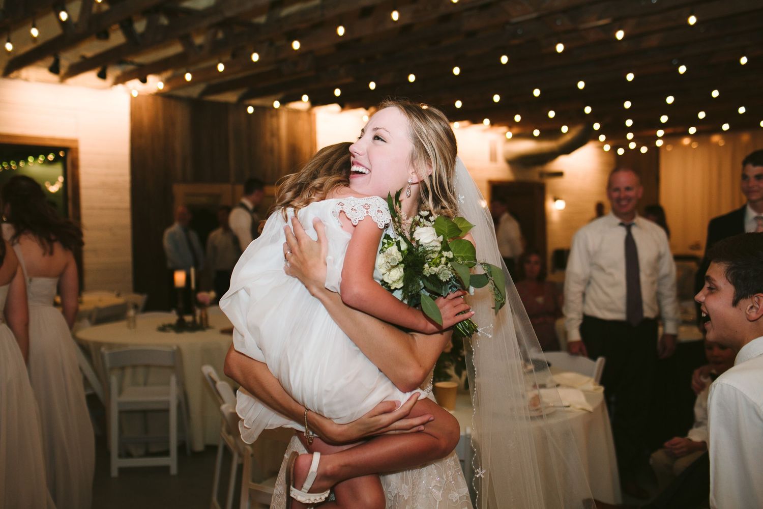 An emotional moment during a wedding reception as someone is embraced under twinkling lights.