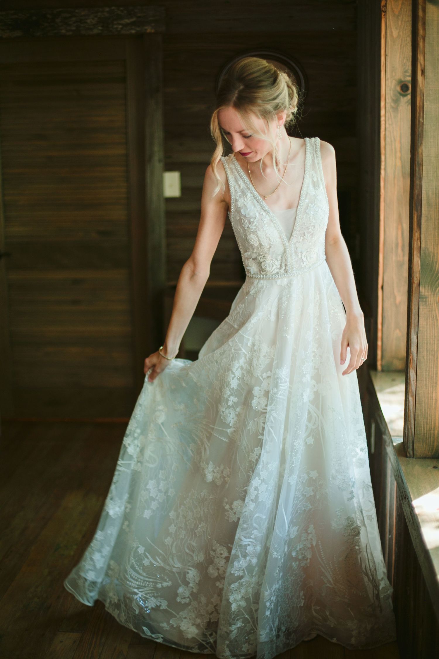 Full-length view of romantic lace wedding gown with flowing skirt in rustic wooden setting.