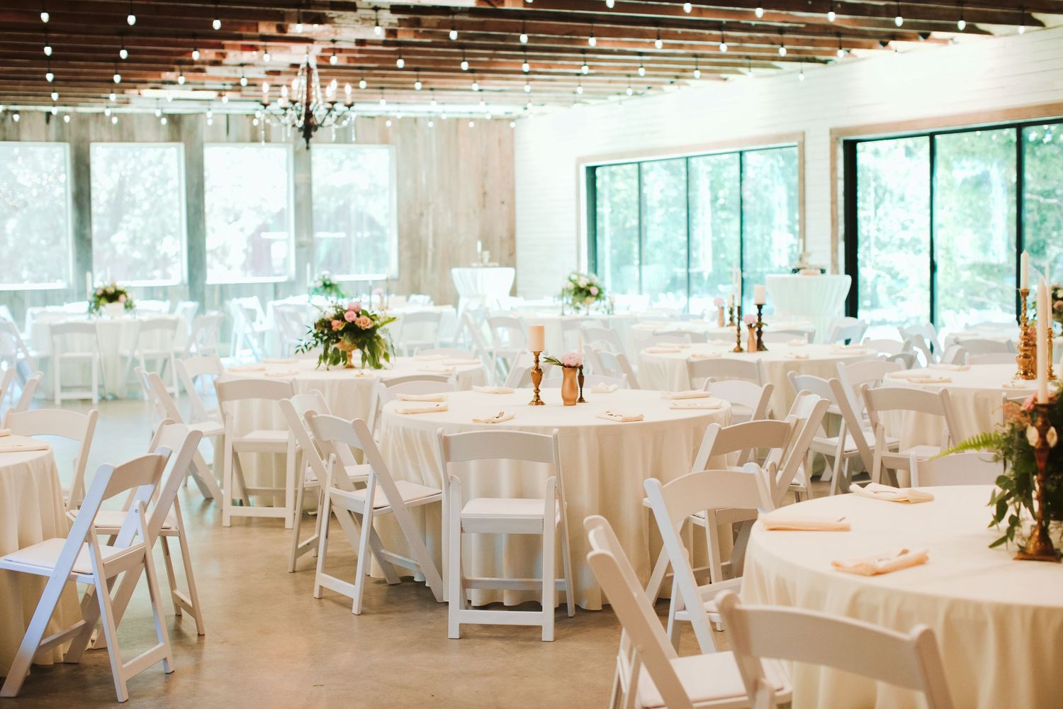 Elegant wedding reception setup with white folding chairs and tables in a bright modern venue.