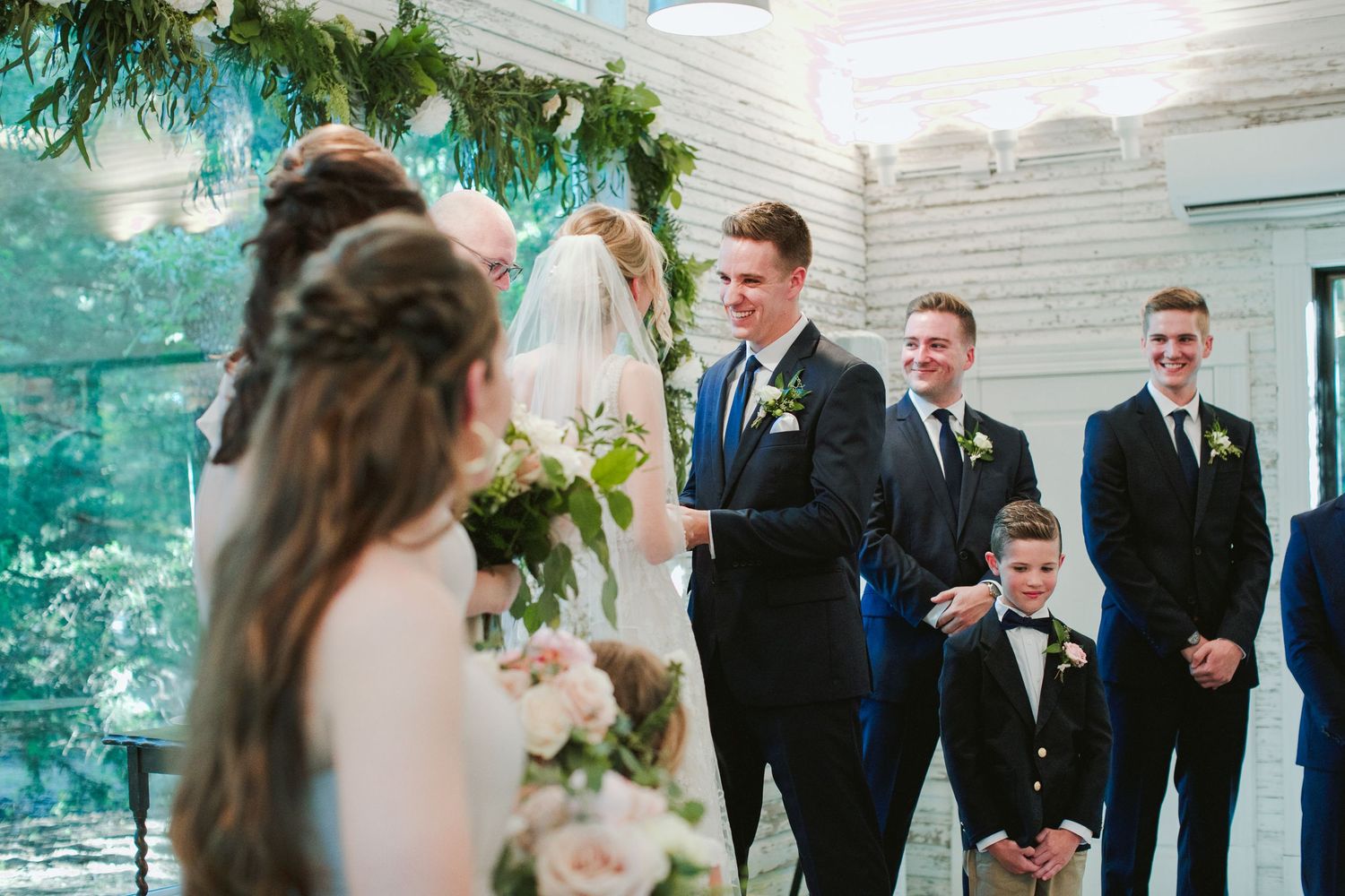 Wedding ceremony in a modern white chapel with groomsmen standing at the altar.