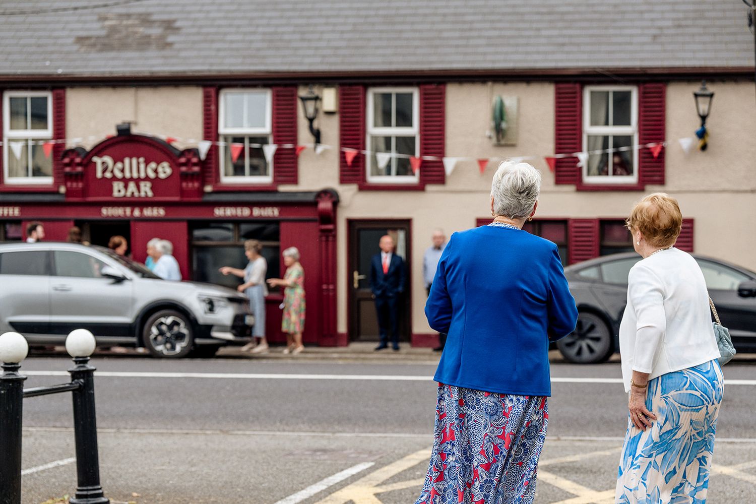 People stand outside a traditional red-painted Irish pub named 'Police Bar' with white window frames on a street corner.