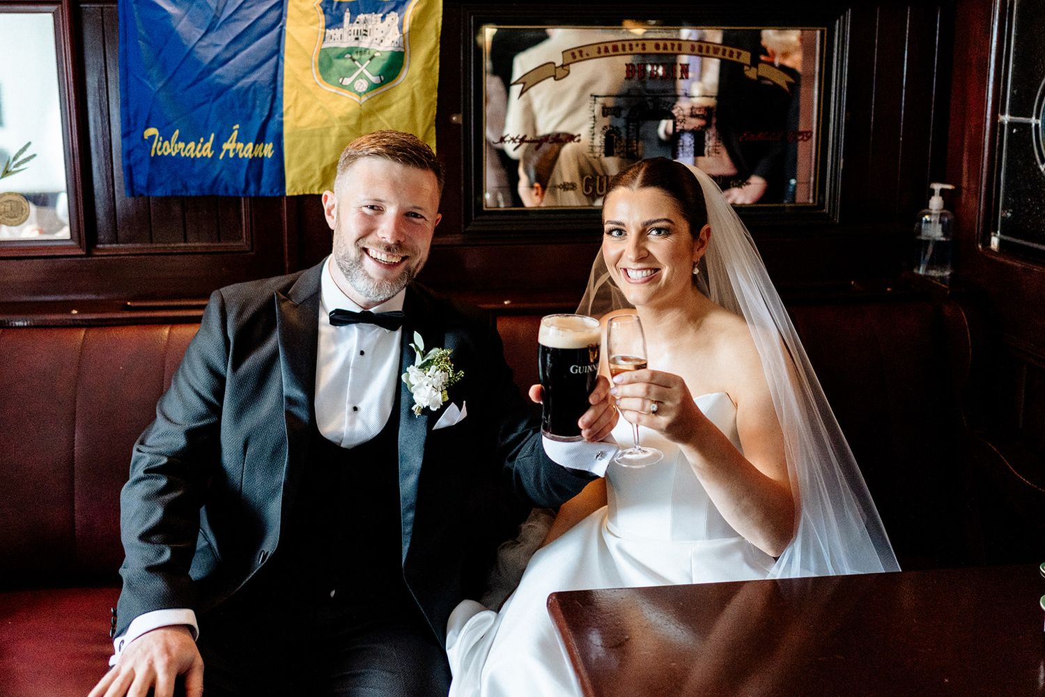 A bride and groom smile while toasting with drinks at a pub on their wedding day.