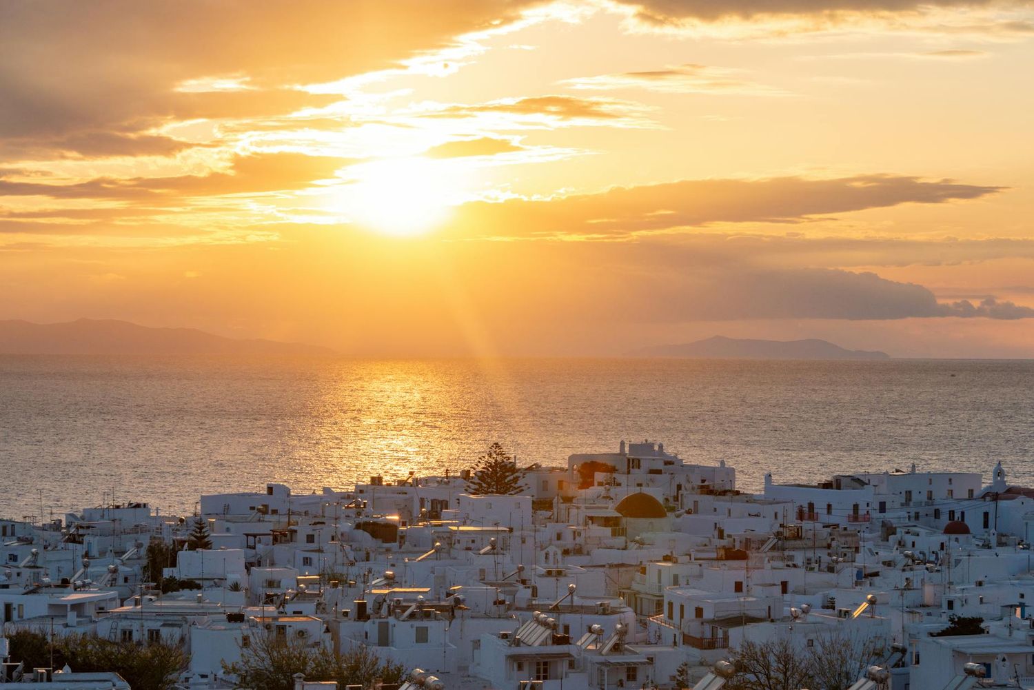 Golden sunset over white buildings of Santorini island with Mediterranean Sea reflecting vibrant orange light. Wedding Photo Wedding Video.