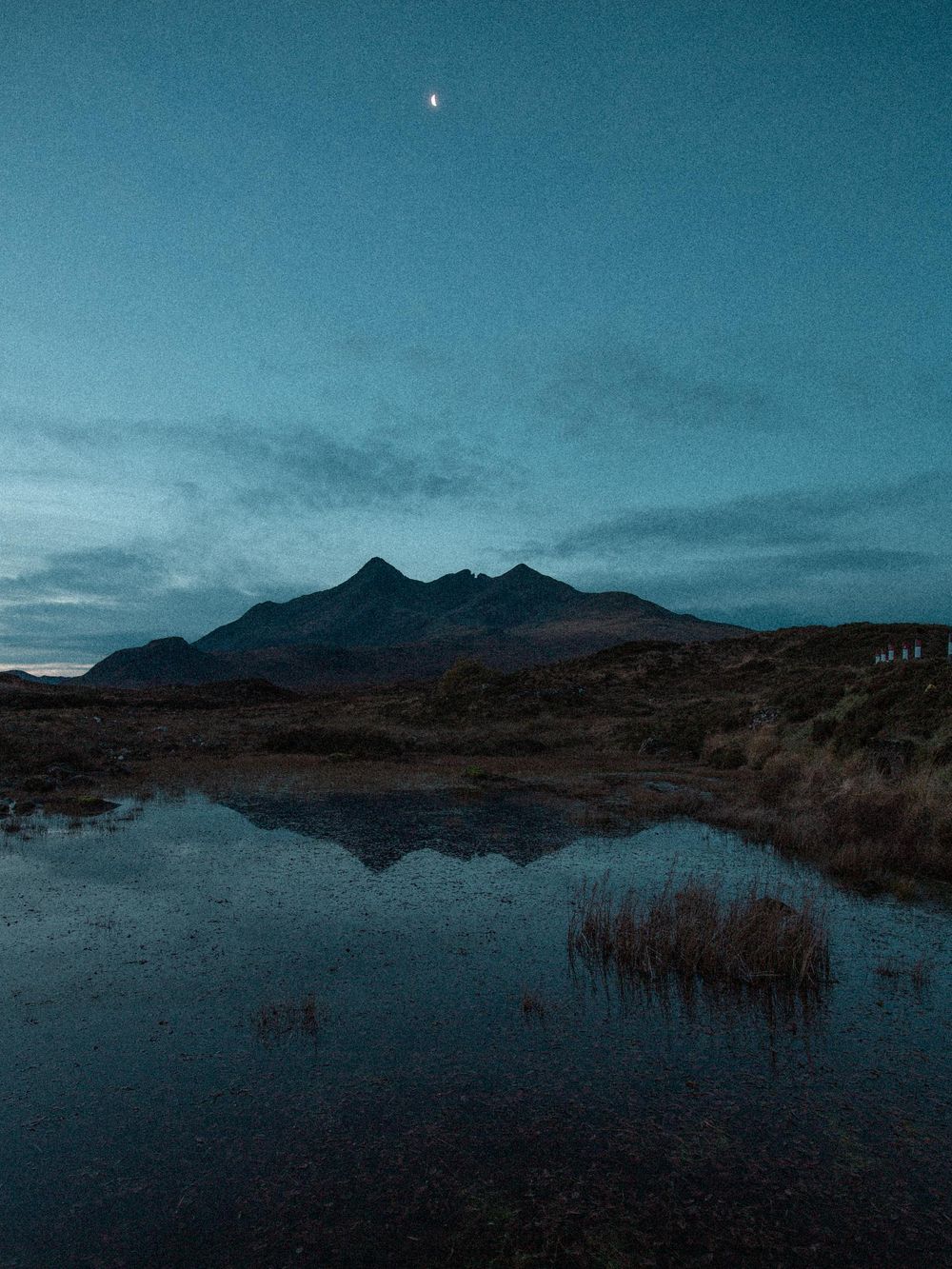 Panoramic view of misty mountains reflecting in a tranquil loch during twilight in the Scottish Highlands.