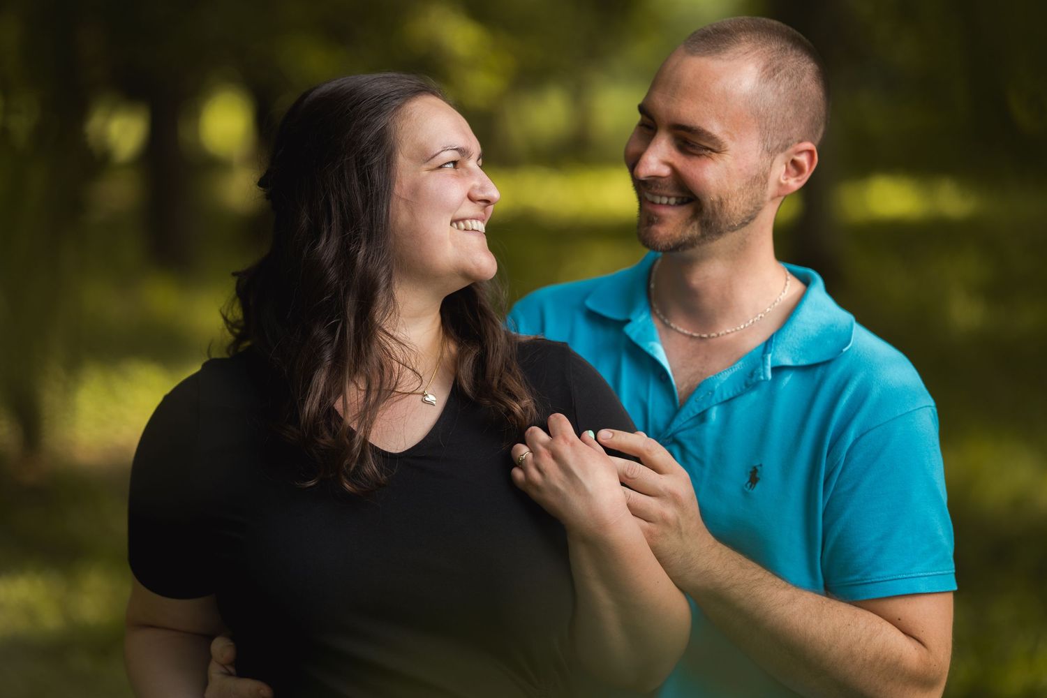 A couple shares a joyful moment together outdoors with natural sunlit trees in the background.