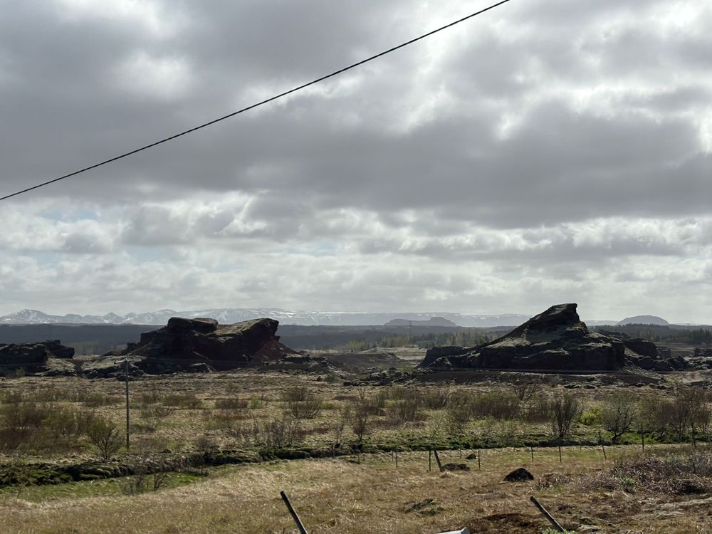 Dark rock formations rise against a cloudy sky in a desert landscape with power lines crossing overhead.