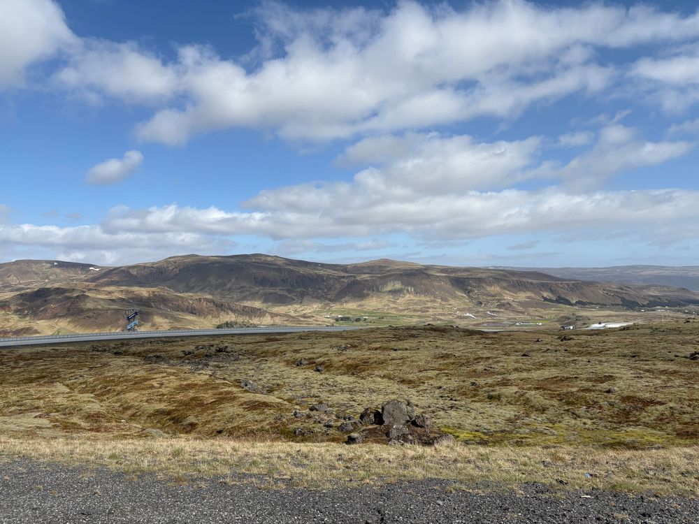 Rolling hills and mountains stretch across a rugged Irish landscape under puffy white clouds and blue sky.