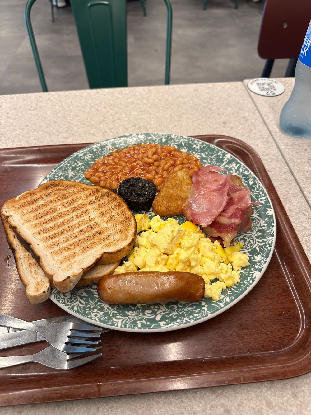 Traditional English breakfast with scrambled eggs, toast, baked beans, grilled sausage and ham on a decorative plate.
