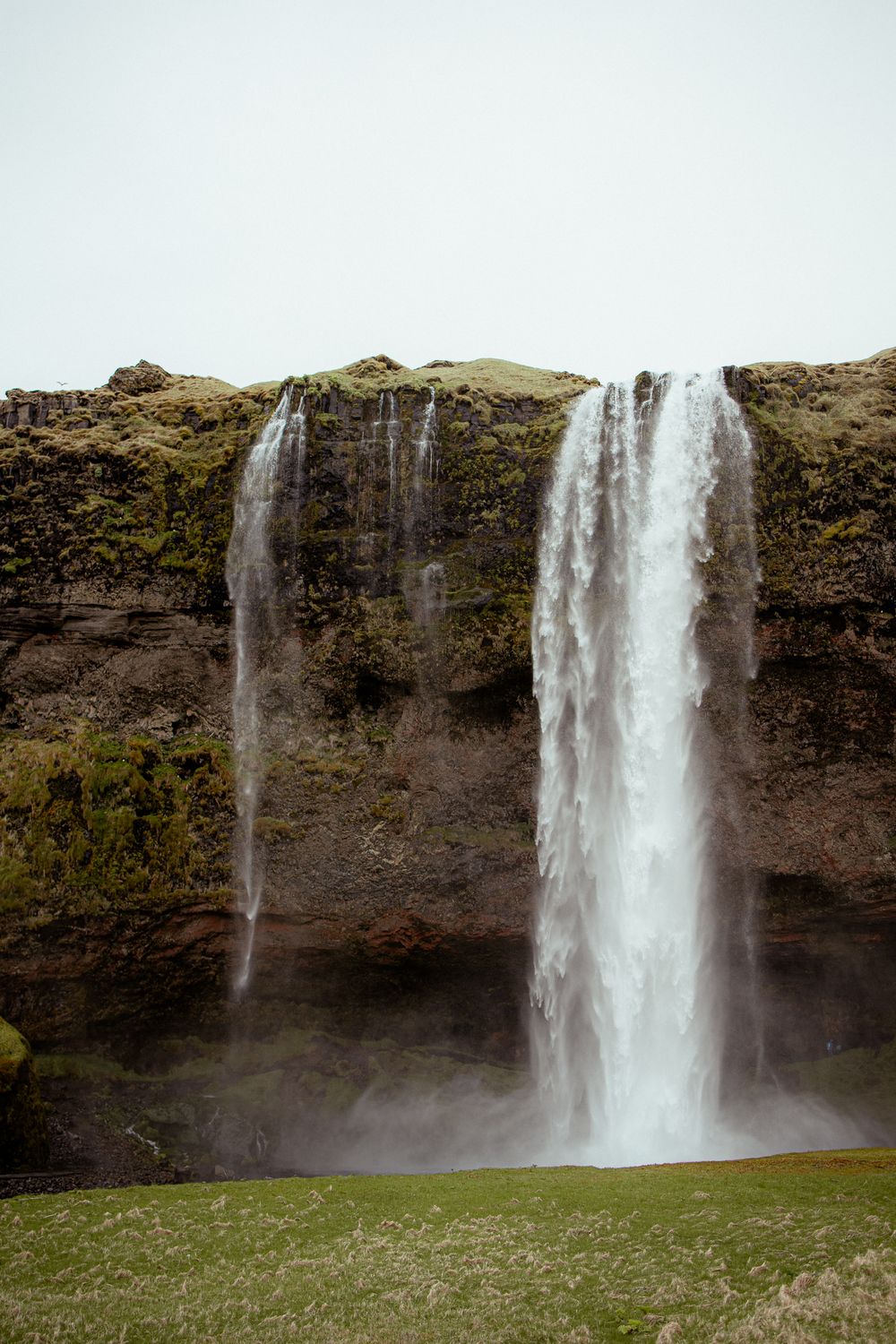 Dramatic waterfall cascades down a steep moss-covered cliff face in Iceland's rugged landscape.