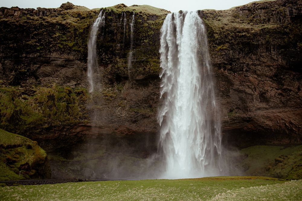Majestic double waterfall cascades down moss-covered cliffs in Iceland, creating a misty natural spectacle.