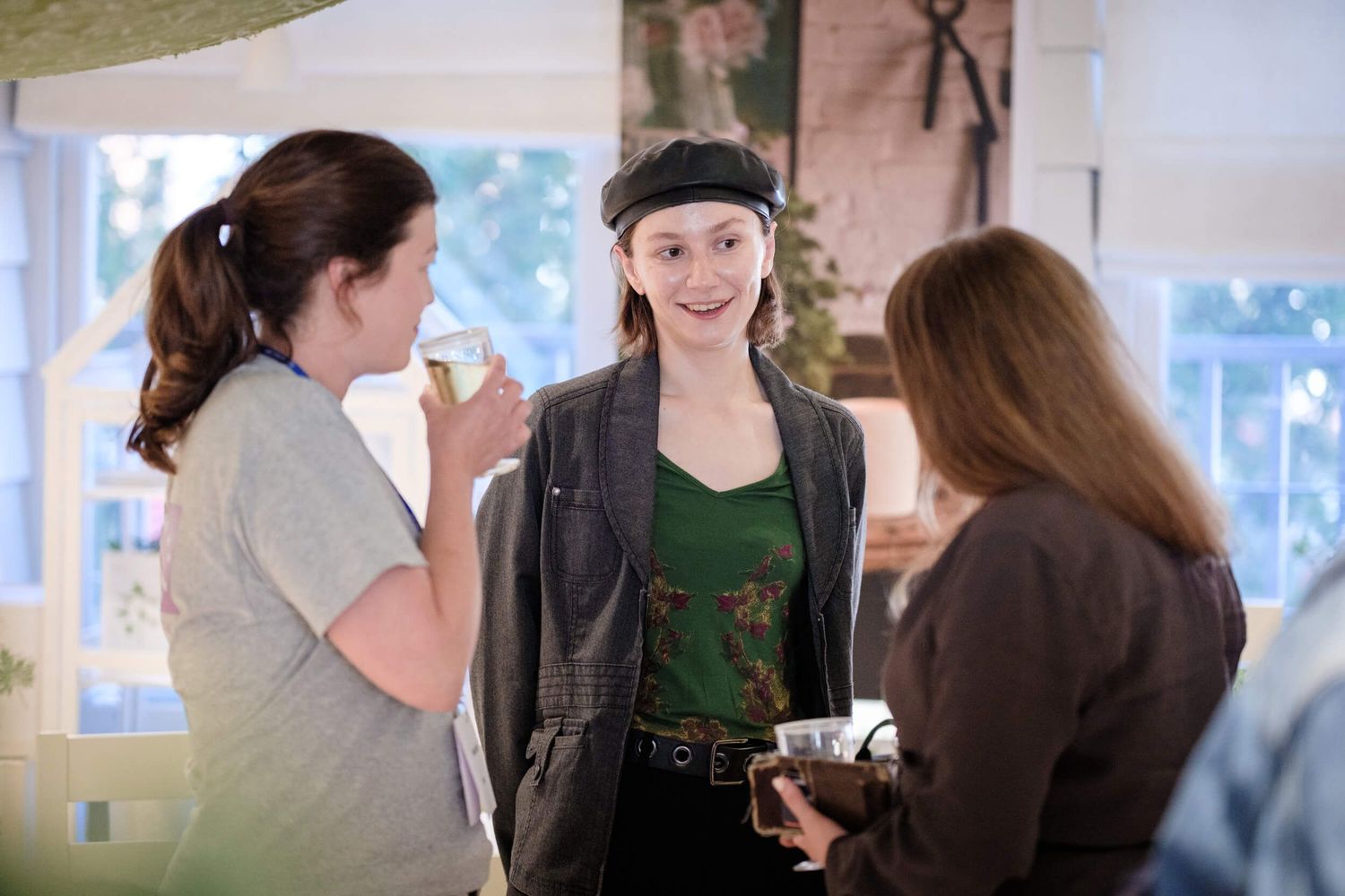 Three people having a casual conversation in a bright indoor space with windows visible in the background.