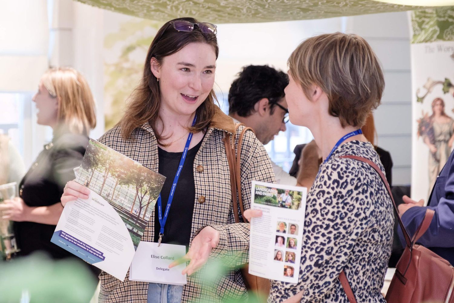Two attendees engage in animated conversation while holding event materials at a networking gathering under a tent.