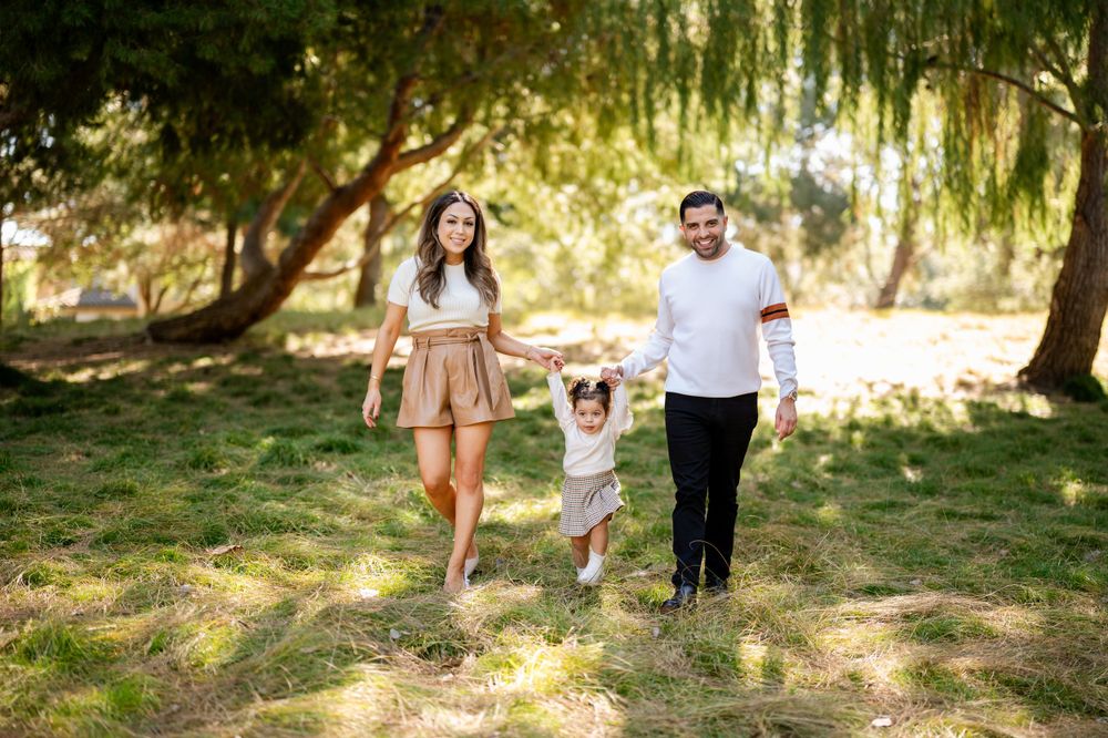 A young family walks together under willow trees in a sunlit park.