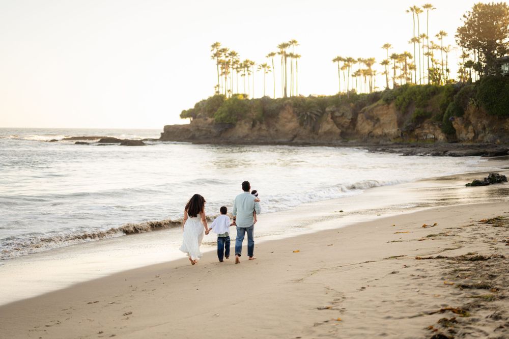 Silhouette of family walking along shoreline at sunset with cliffs in background.