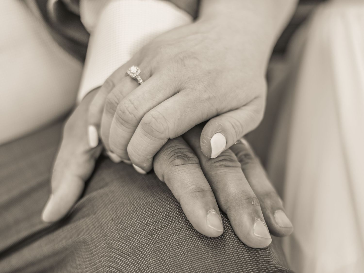 Close-up black and white photo of hands with engagement ring resting on fabric.