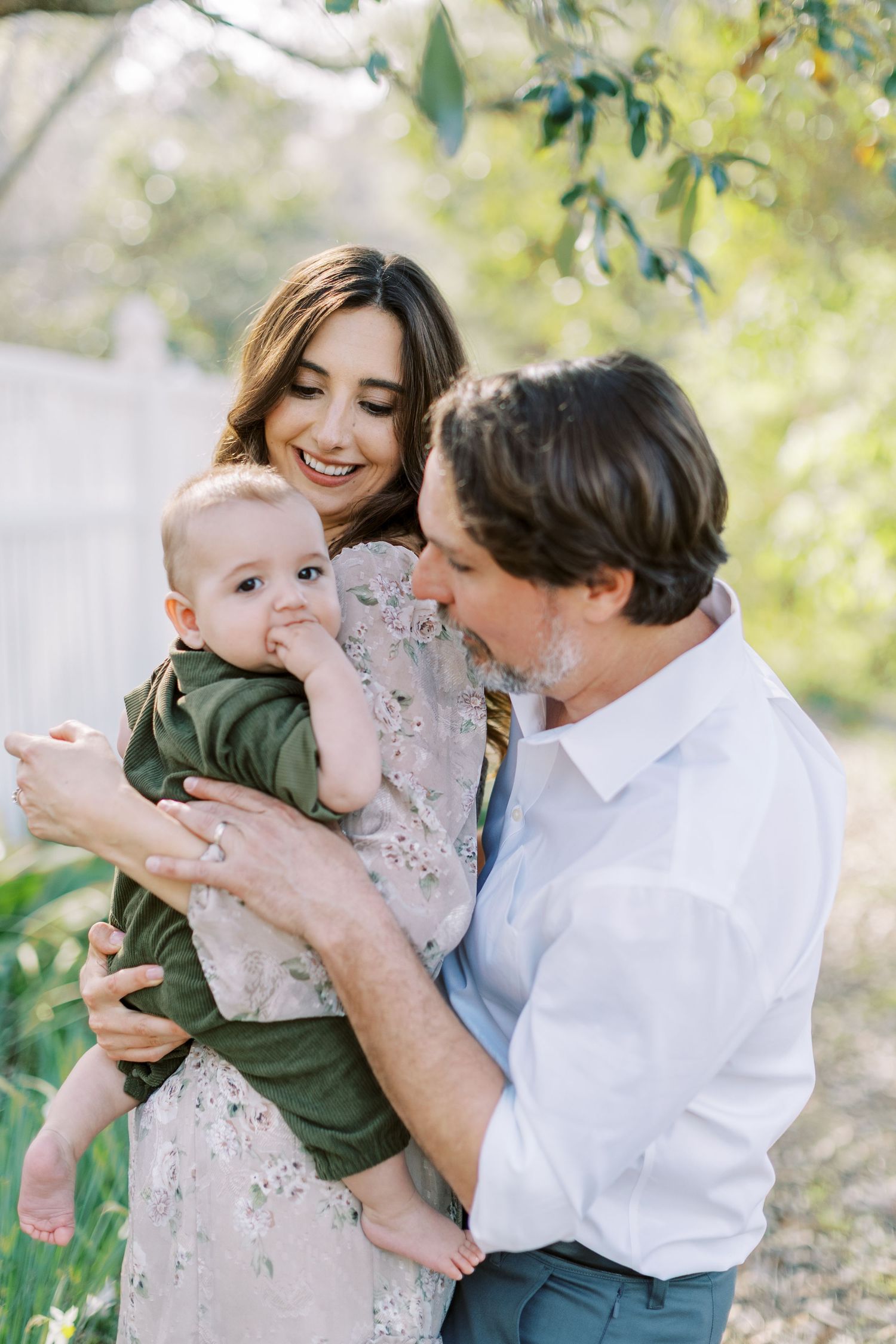 A young family shares a joyful moment together outdoors on a sunny day with green foliage in the background.