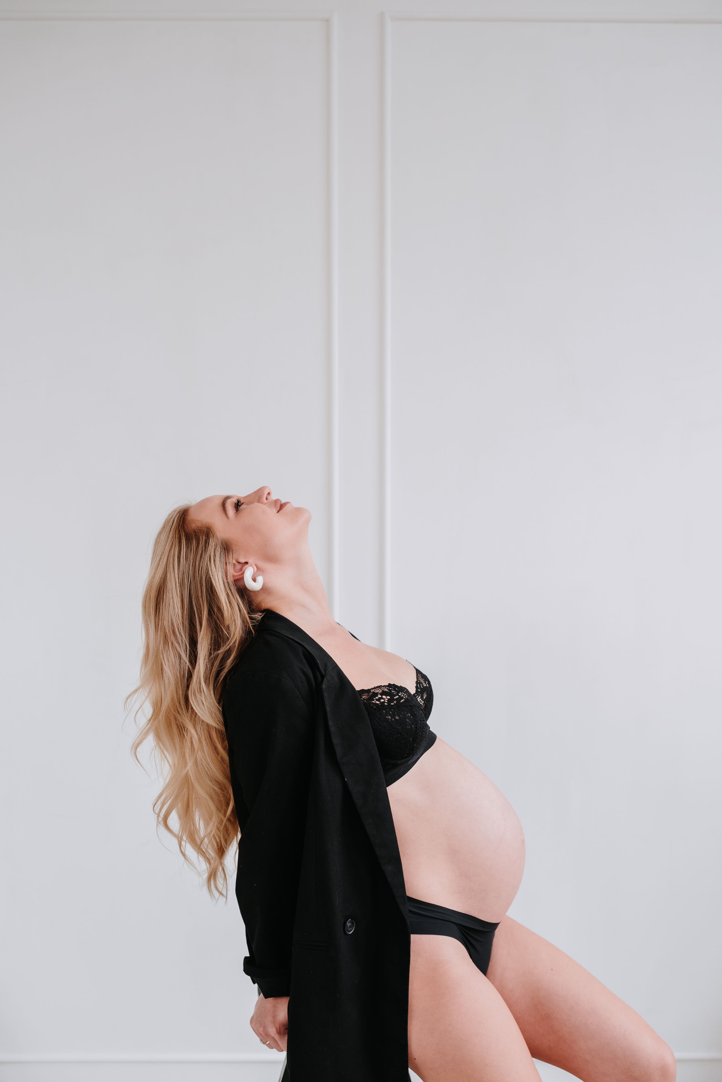 A person wearing a black cardigan leans back dramatically against a white wall with flowing blonde hair.