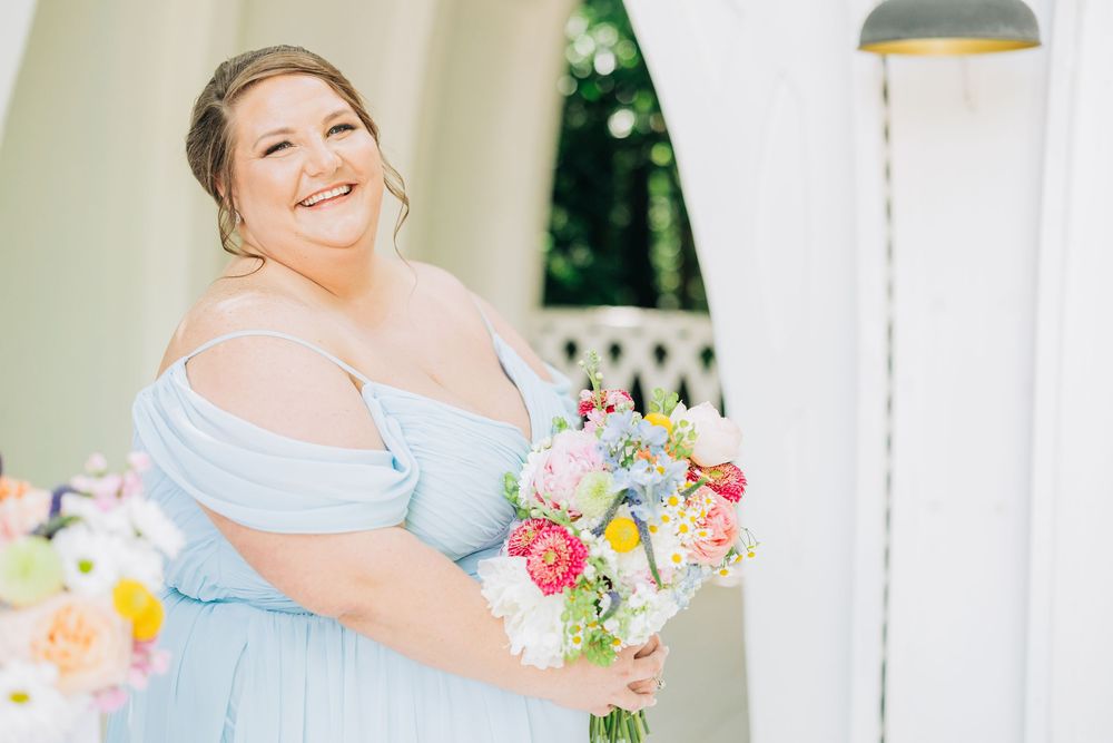 A bride in a light blue off-shoulder dress holds a vibrant spring bouquet on a bright sunny day.