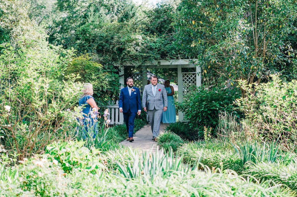 People walking together on a lush green garden path surrounded by trees and vegetation.