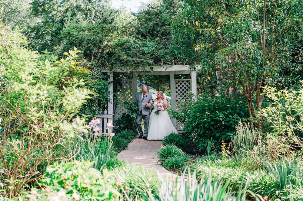 A lush garden path with green foliage and white garden structures creates a serene outdoor setting.