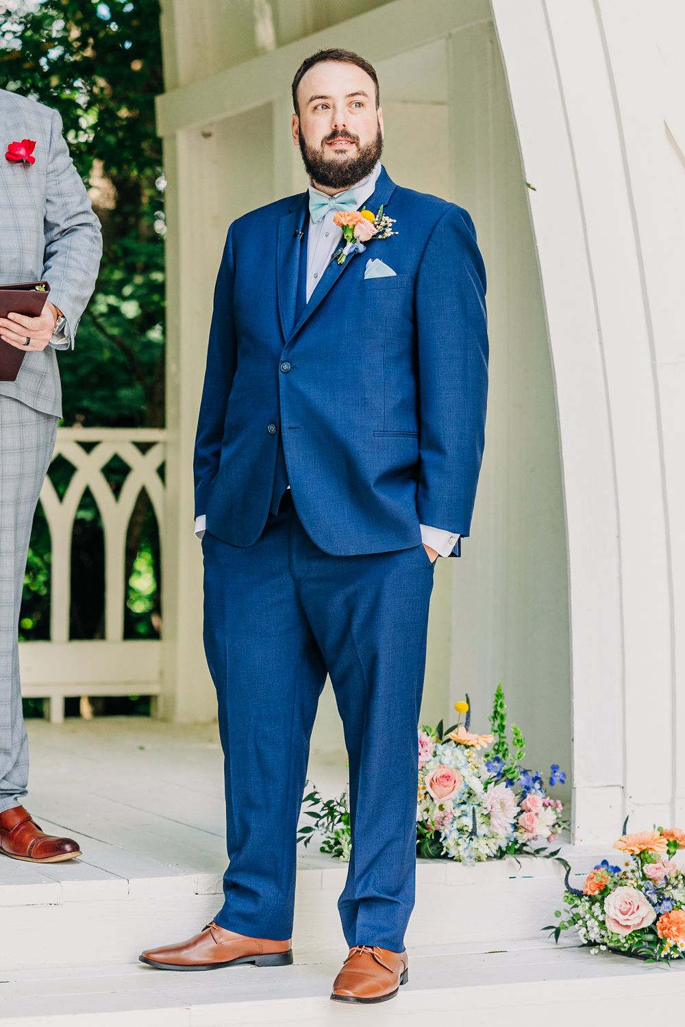 Multiple views of a groom in a navy blue suit and brown shoes posing in an elegant white gazebo with floral decor.