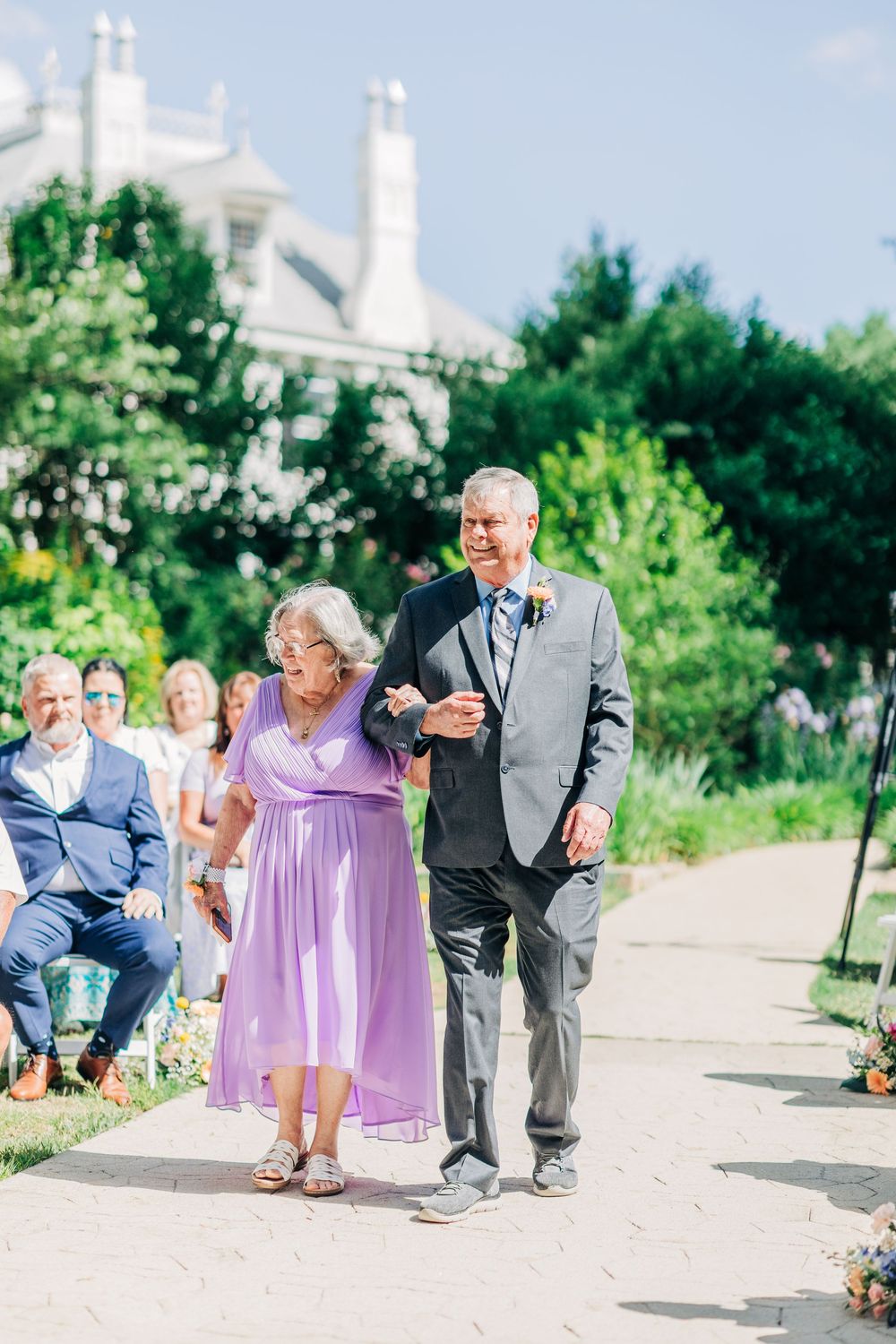 Light and airy sequence shots of wedding guests in purple dresses walking outdoors at a summer celebration.
