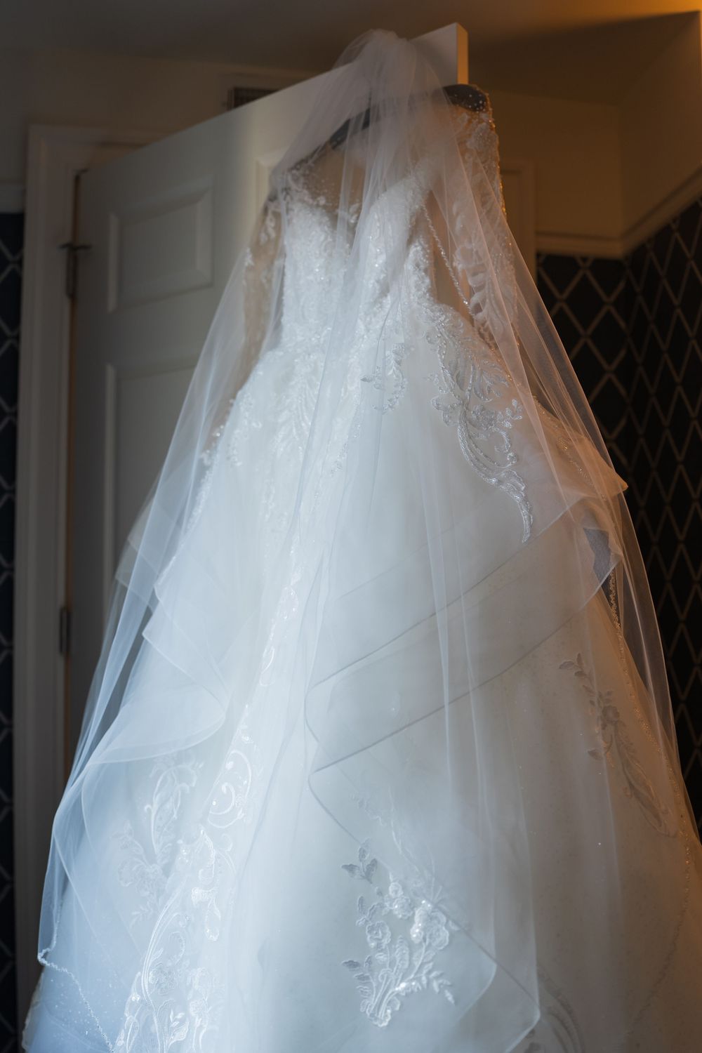 Wedding dress with full tulle skirt and lace bodice hangs elegantly against white doors.
