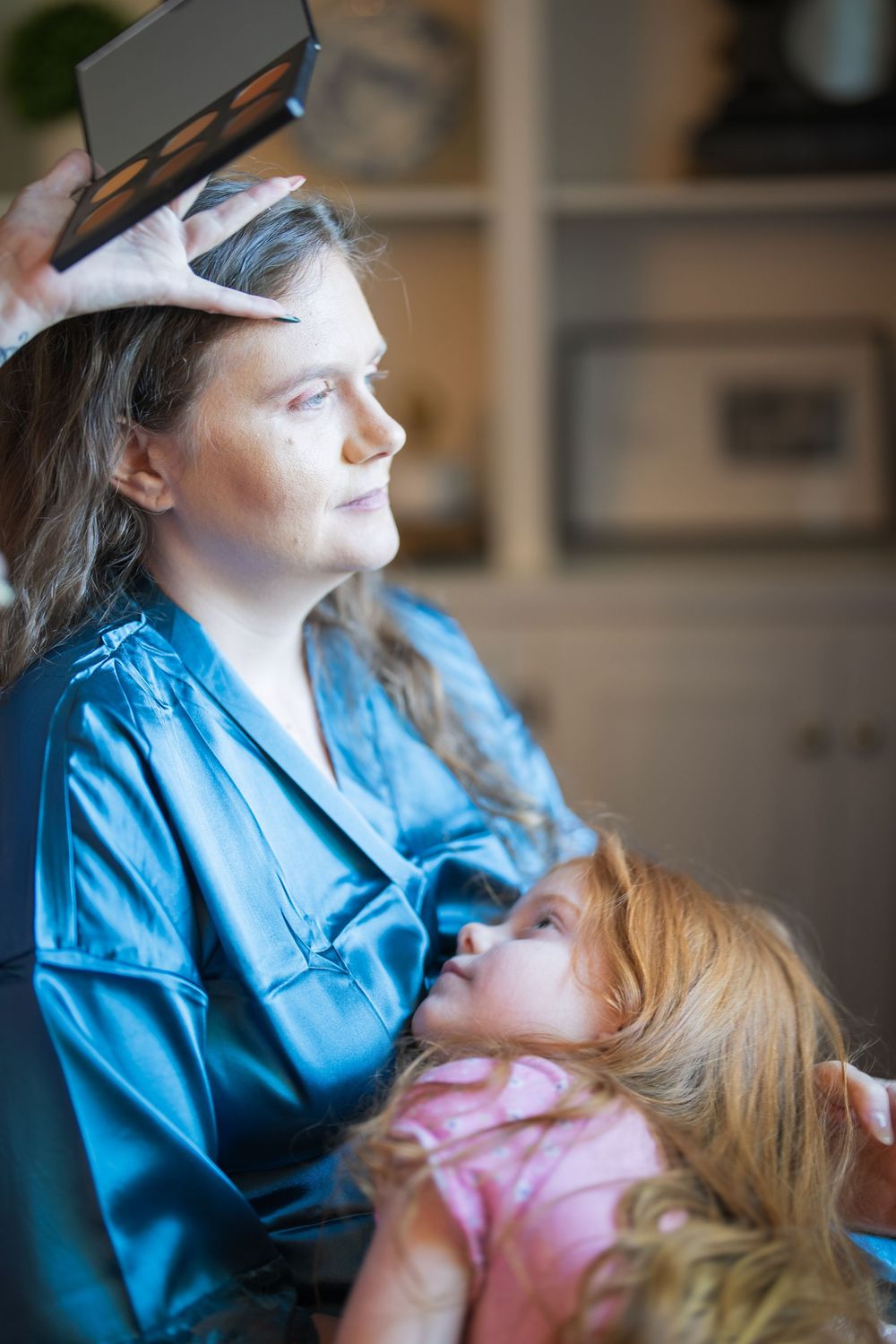 A person in a blue satin robe looks to the side while another in pink sits nearby.