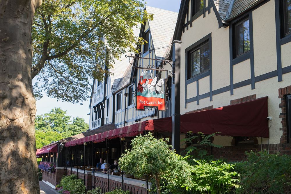Tudor-style buildings with red awnings line a charming shopping street on a sunny day.