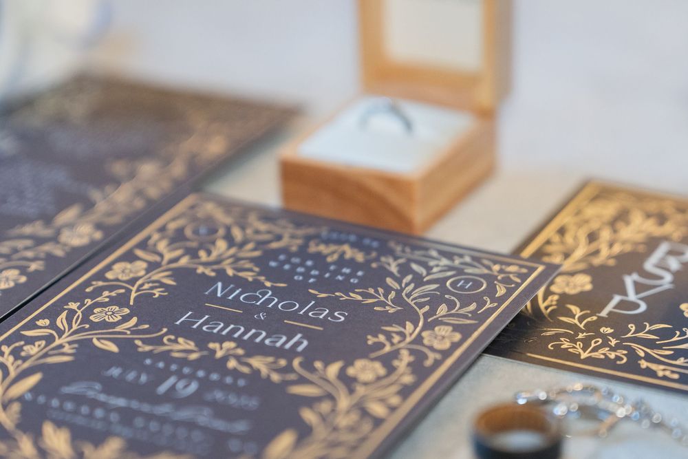 Close-up of elegant gold foil wedding invitations with ornate decorative patterns and text on light backgrounds.